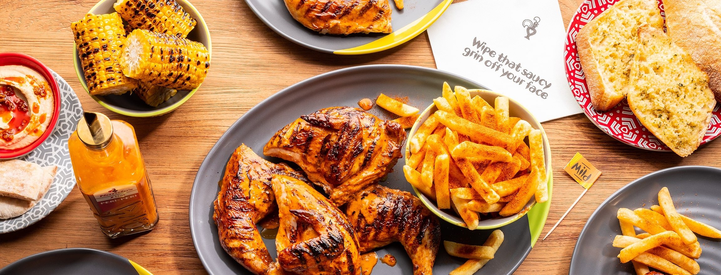 a Nando’s meal on a table including PERi-PERi chicken, a salad, chips, and a selection of sides