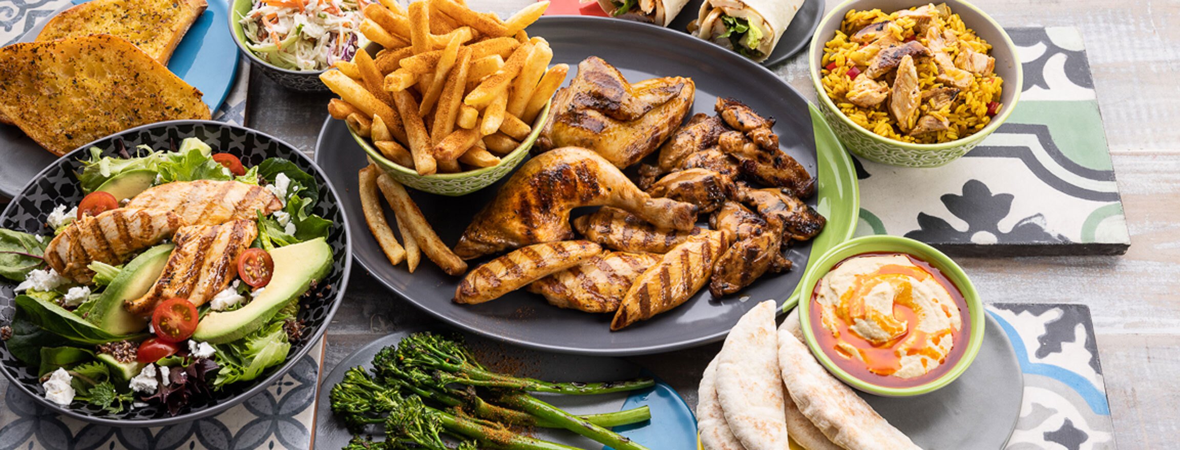 a Nando’s meal on a table including PERi-PERi chicken, a salad, chips, and a selection of sides