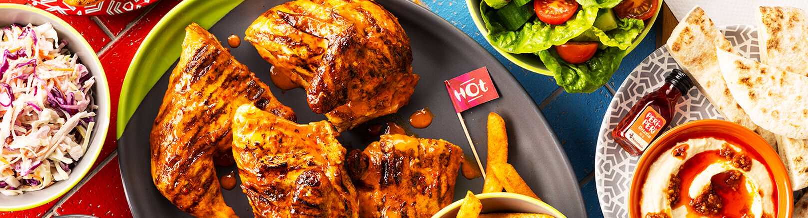 a Nando’s meal on a table including PERi-PERi chicken, a salad, chips, and a selection of sides